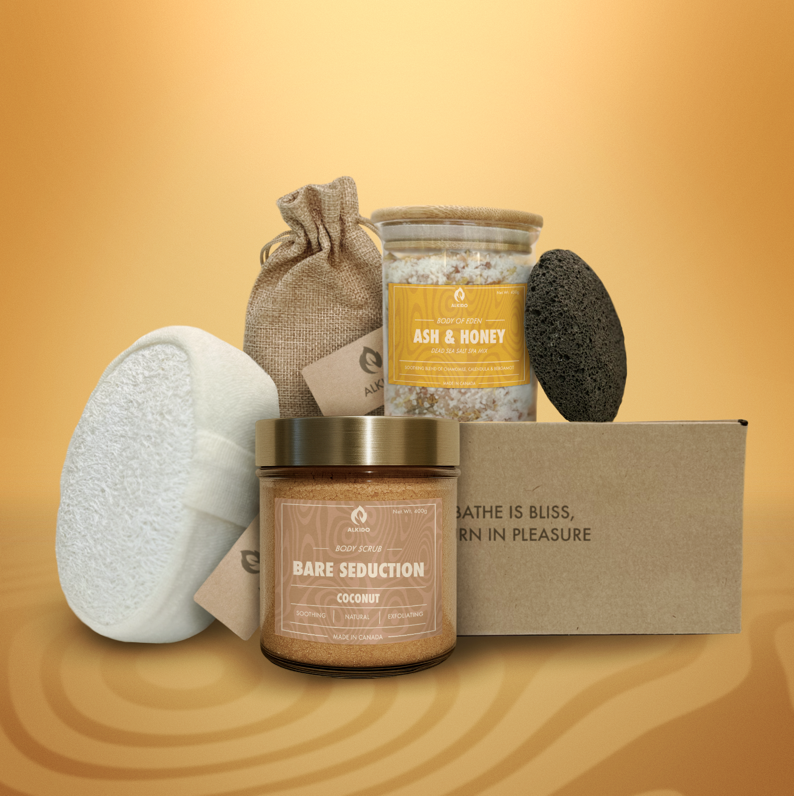 ALKIDO spa gift set featuring 'Bare Seduction' coconut body scrub, 'Ash & Honey' Dead Sea salt spa mix, lavender sachet in linen bag, natural loofah, and black lava stone, arranged with a branded box on a warm amber background.