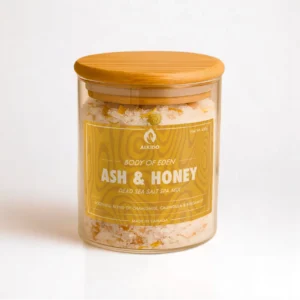 ALKIDO Ash honey spa salt mix in a clear glass jar with a wooden lid and red label, topped with dried chamomile, calendula on a light background