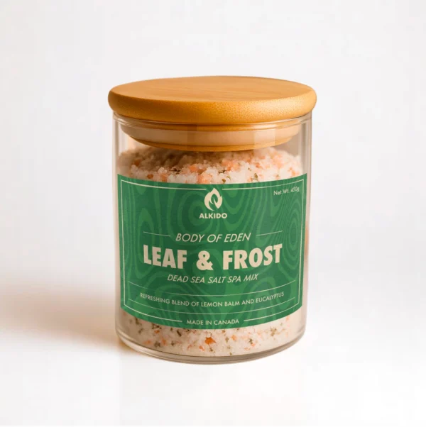 ALKIDO Leaf frost spa salt mix in a clear glass jar with a wooden lid and green label, topped with dried lemon balm, on a light background